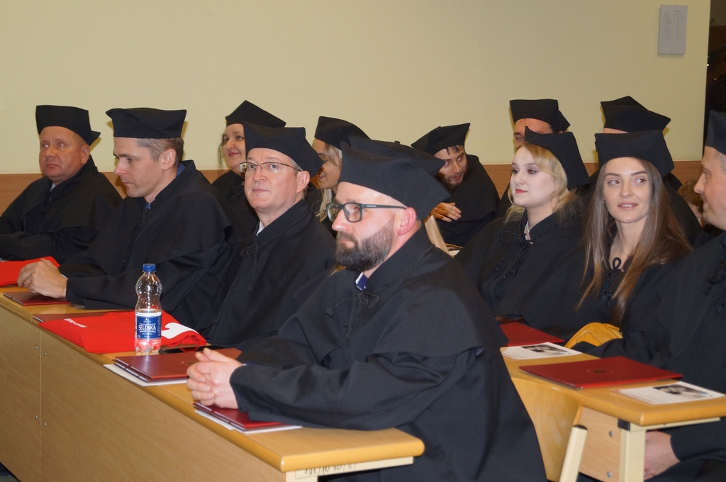 studenci siedzący w ławach w togach 