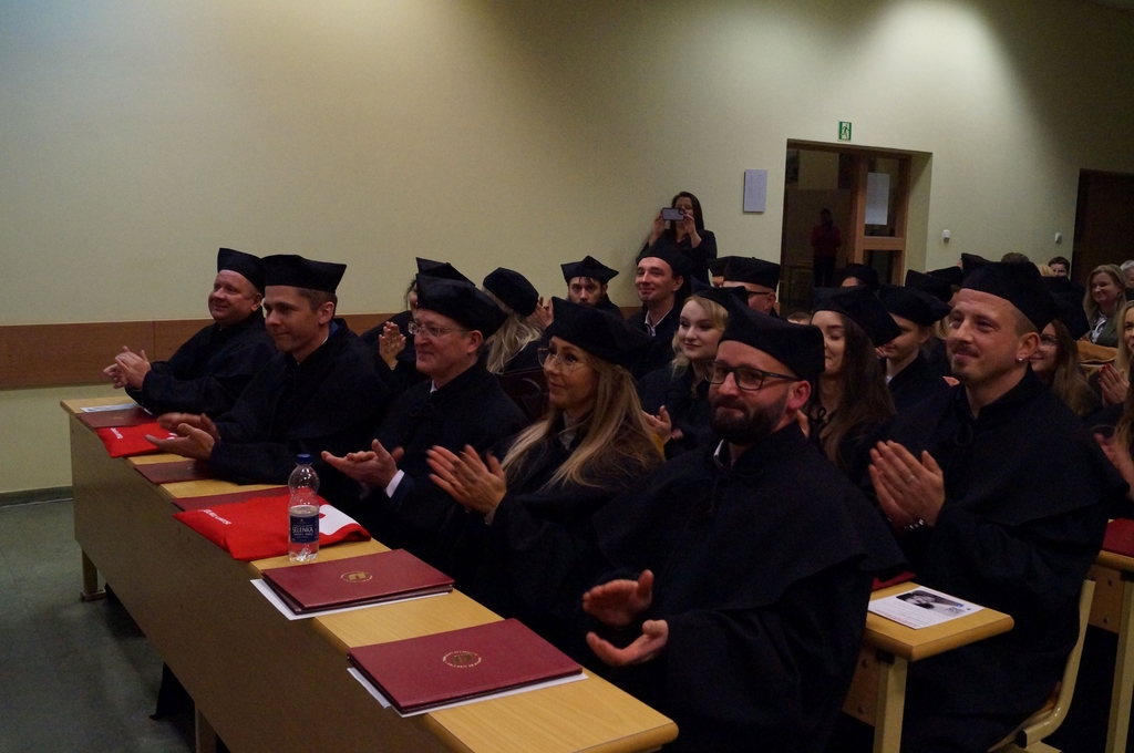 studenci siedzacy w ławach ubrani w togi absolwentów