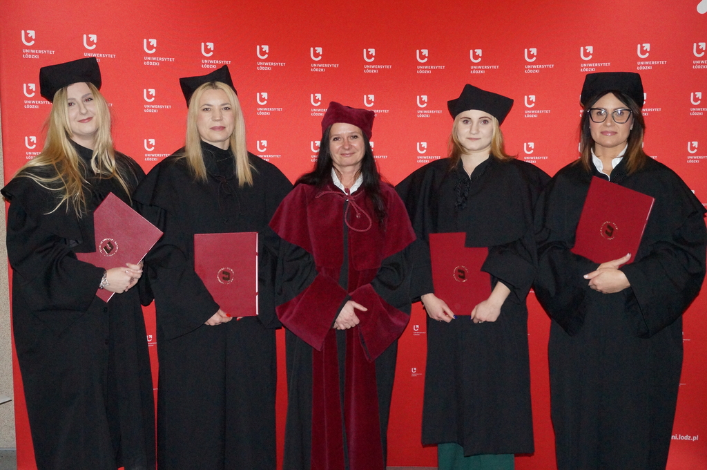 Zdjęcie absolwentów ubranych w birety i togina czerwonej ściance z logami uniwersytetu łódzkiego