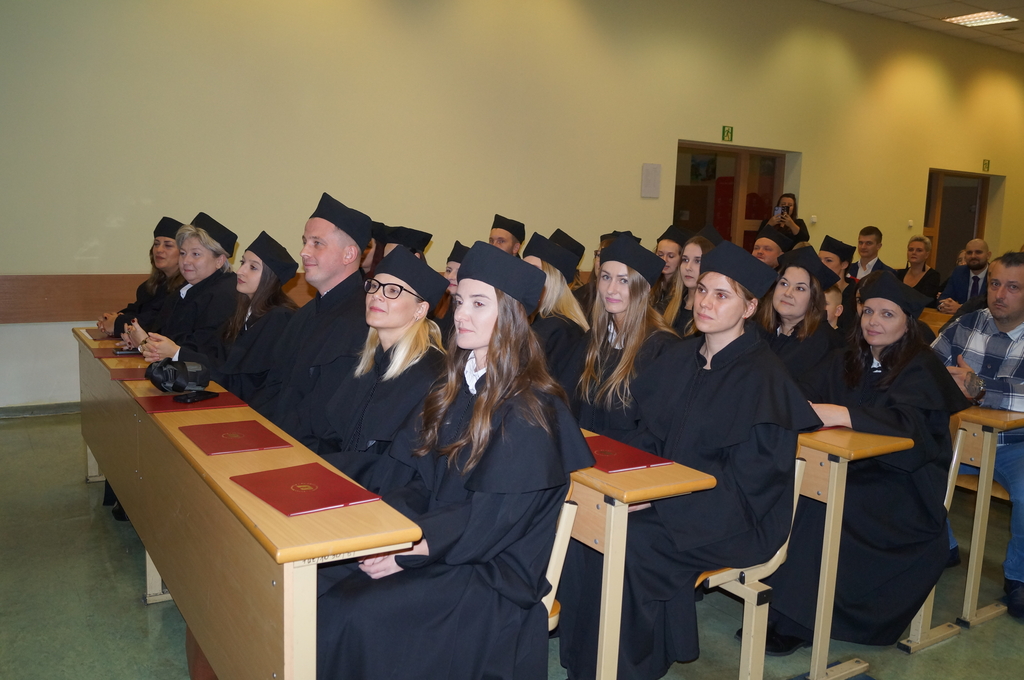 absolwenci siedzący w ławach na auli podczas gali