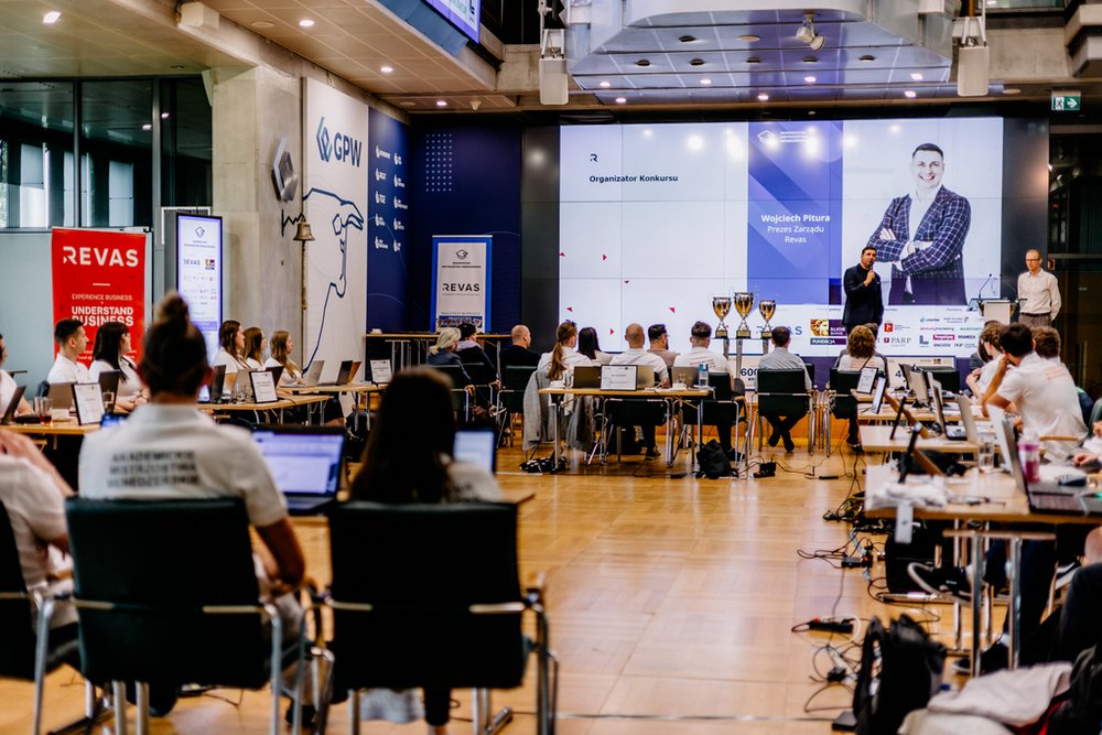 zdjęcie zrobione podczas wykładu w trakcie twania konkursu w głębi scena z prelegentem na pierwszym planie uczestnicy
