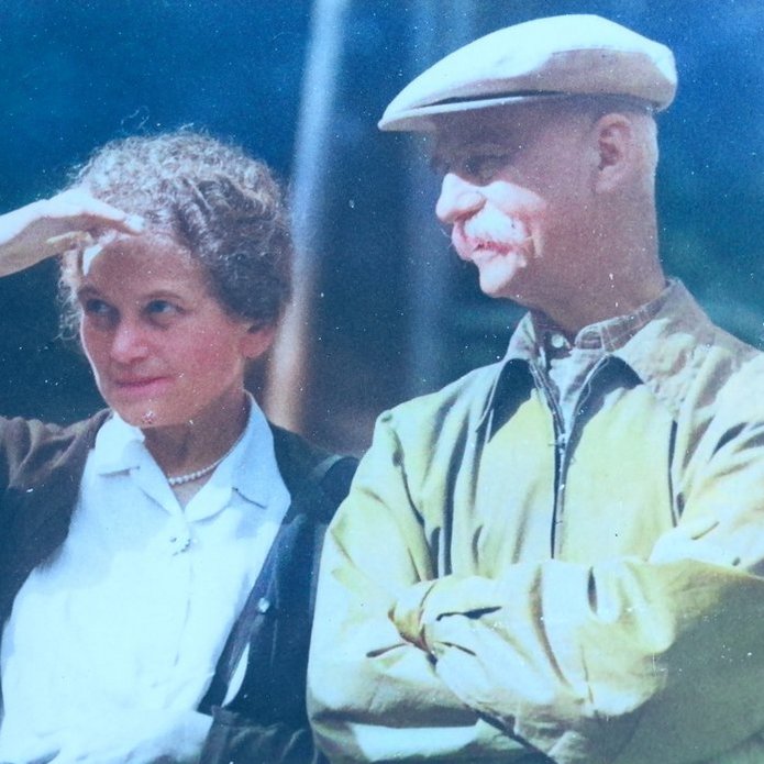 Na zdjęciu widać mężczyznę i kobietę stojących i patrzących przed siebie. Kobieta trzyma prawą dłoń nad czołem i przysłania oczy przed ostrym słońcem, którego blask widoczny jest na zdjęciu.