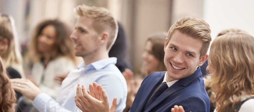 Uśmiechnięci młodzi ludzie siedzący w sali i bijący brawo
