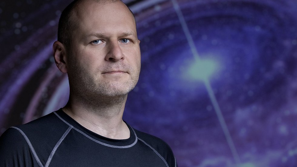 dr Michał Szanecki na tle zdjęcia z gwiazdą neutronową